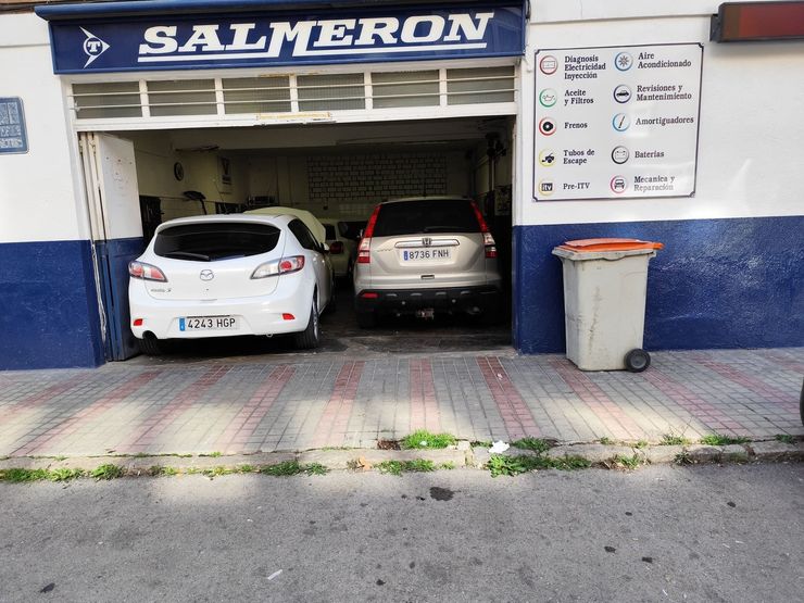 Dos coches aparcados en el garaje de un local comercial en Salmeron, con una acera y un contenedor de basura en el exterior.