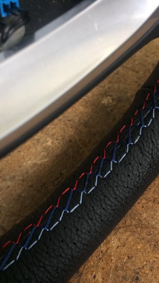 Detalhe de um material texturizado preto com costuras vermelhas, brancas e azuis próximo a uma superfície metálica.