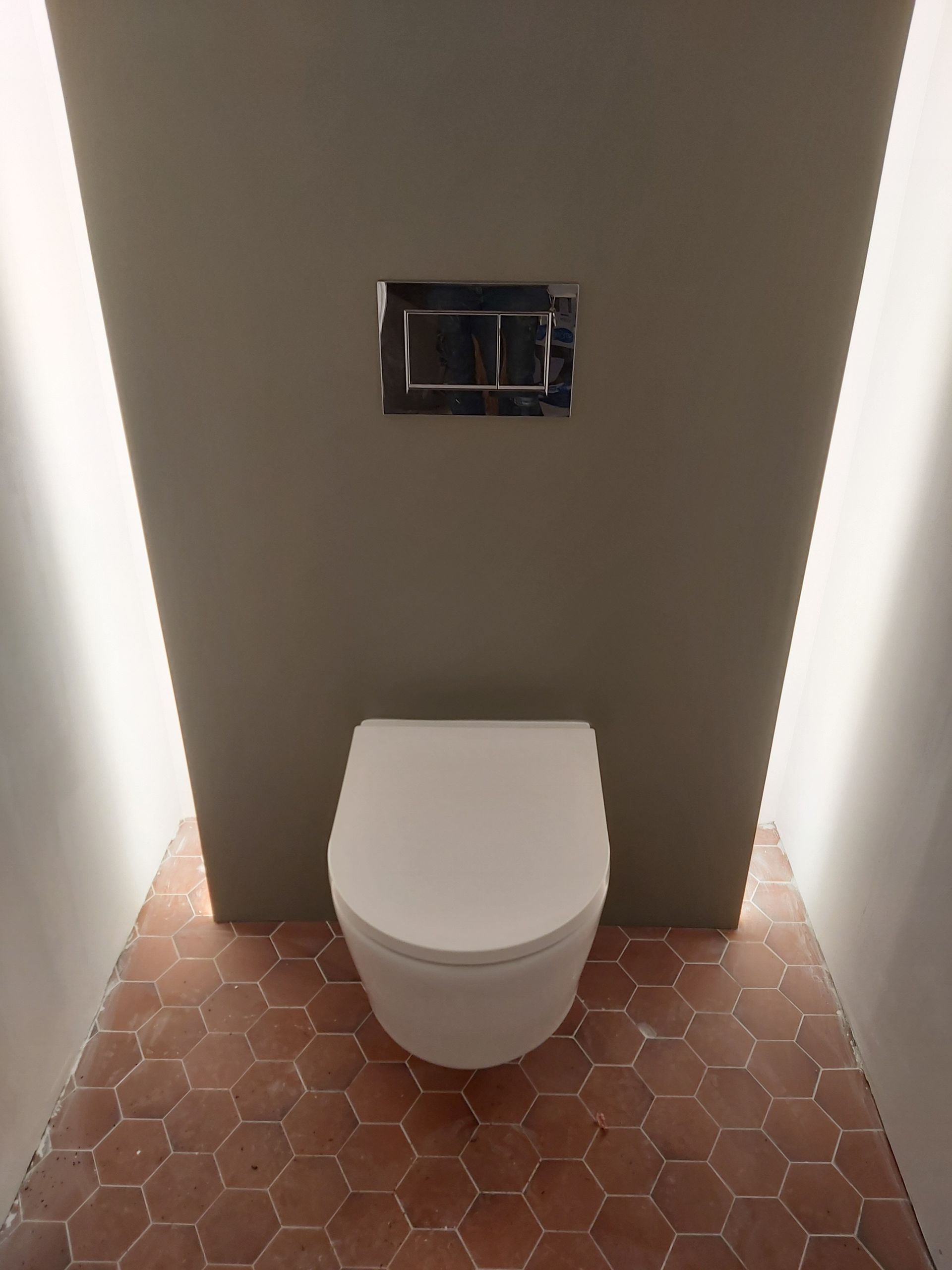 Un plombier raccorde des tuyaux d'eau bleus à un collecteur de plomberie mural avec des raccords rouges et en laiton.