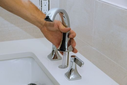 Une main installe un robinet de salle de bains chromé au-dessus d'un lavabo blanc