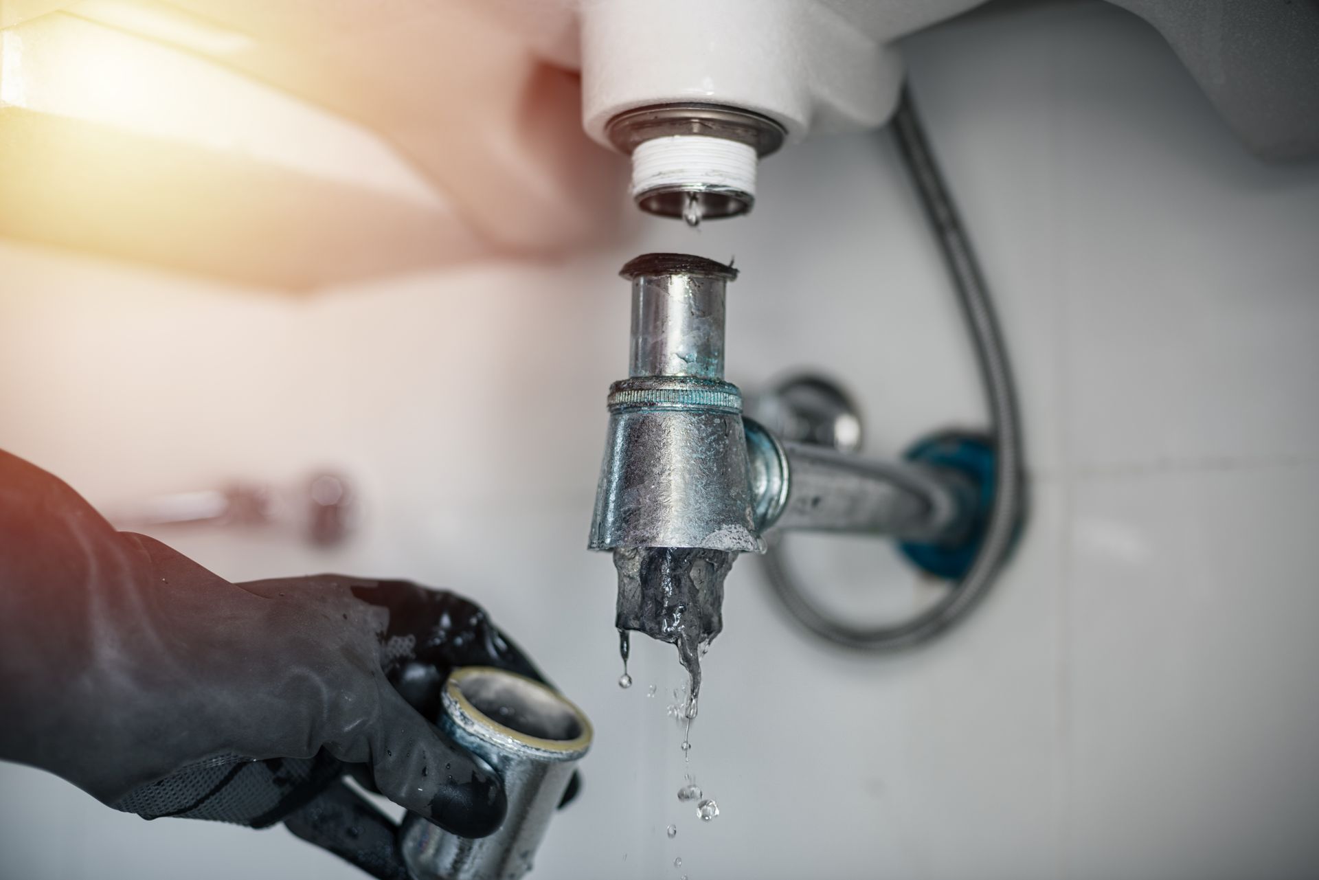 Main gantée de noir resserrant un robinet chromé qui fuit.