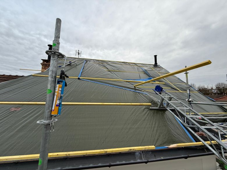 Un toit pentu en construction, recouvert de bâches imperméables grises, de poutres de soutien en bois et d'échafaudages métalliques.