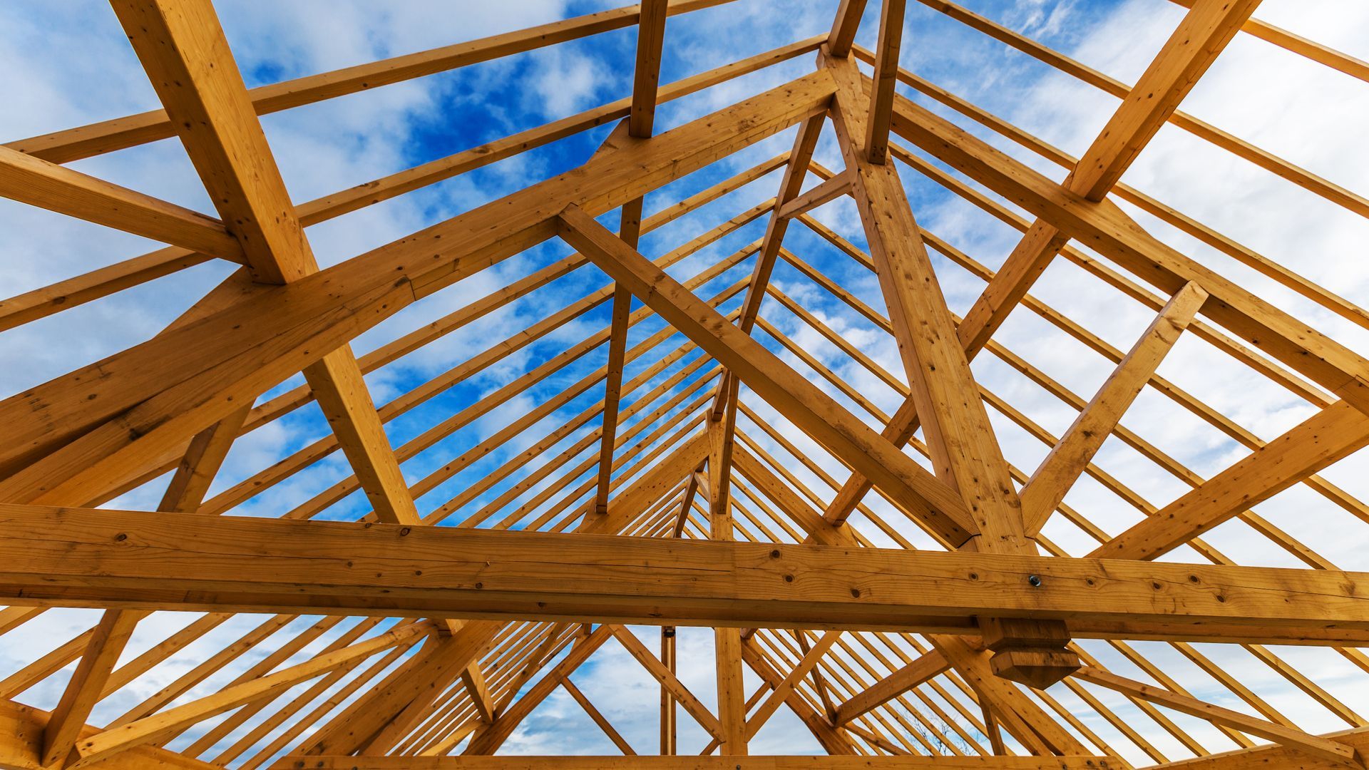 La charpente en bois d'un toit en construction se détache sur un ciel bleu nuageux.
