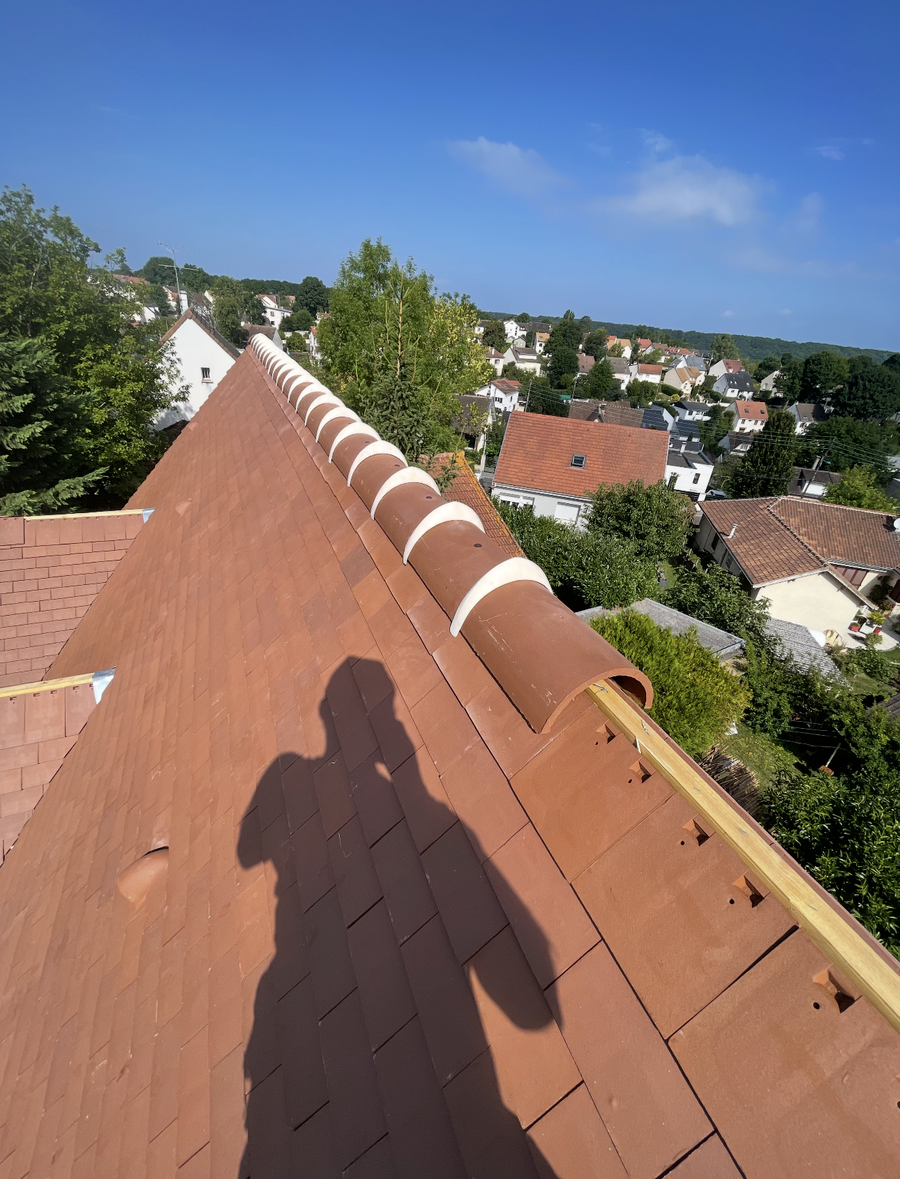 L'ombre d'une personne projetée sur un toit de tuiles en terre cuite dont la ligne de faîtage est ornée de chapeaux de céramique arrondis.