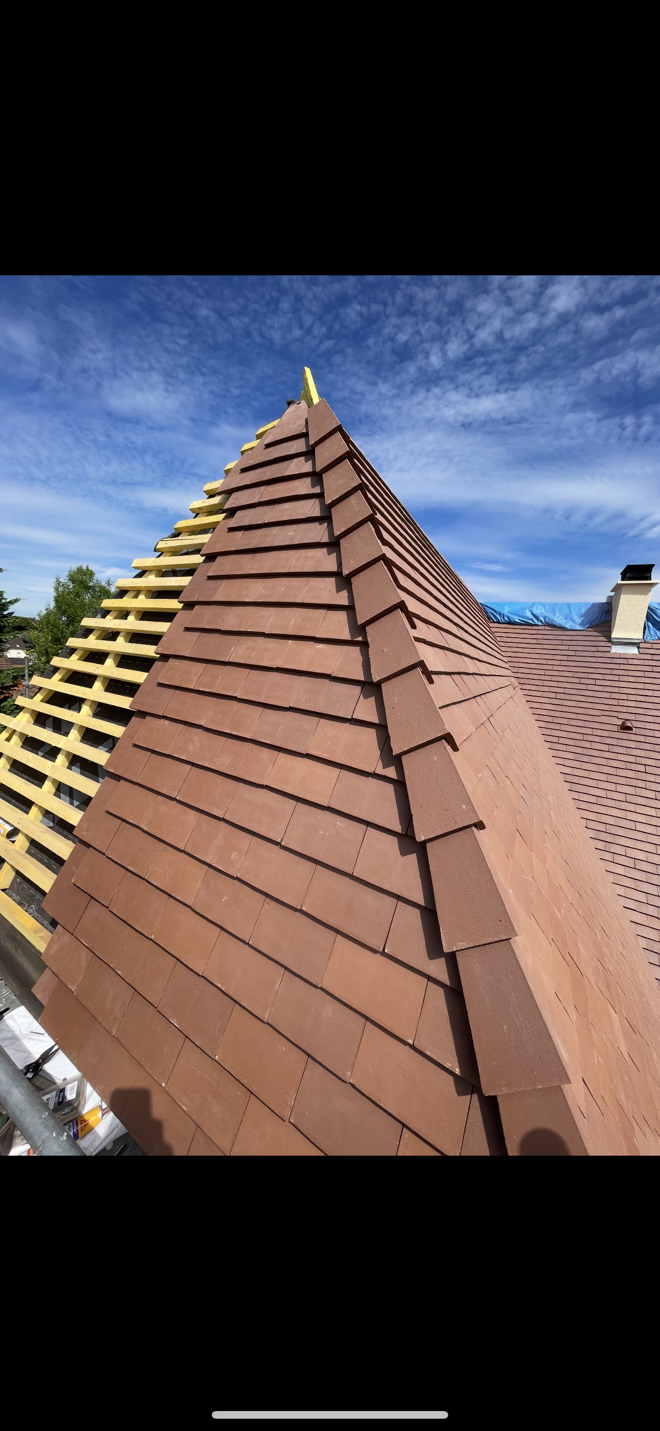 Un toit partiellement couvert de tuiles avec une arête vive, laissant apparaître des tuiles brunes finies d'un côté et des chevrons en bois apparents de l'autre.