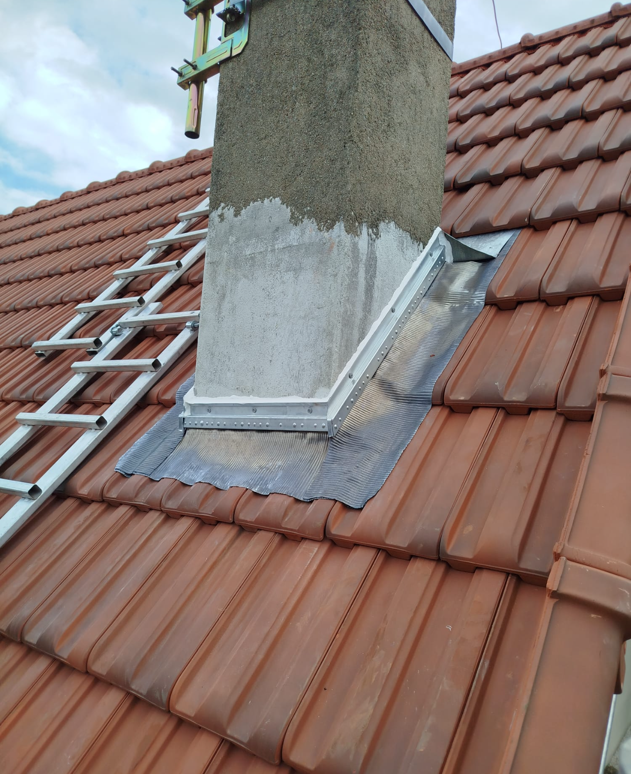 Gros plan sur une cheminée en briques sur un toit de tuiles, montrant les récentes réparations de solins en plomb autour de sa base.