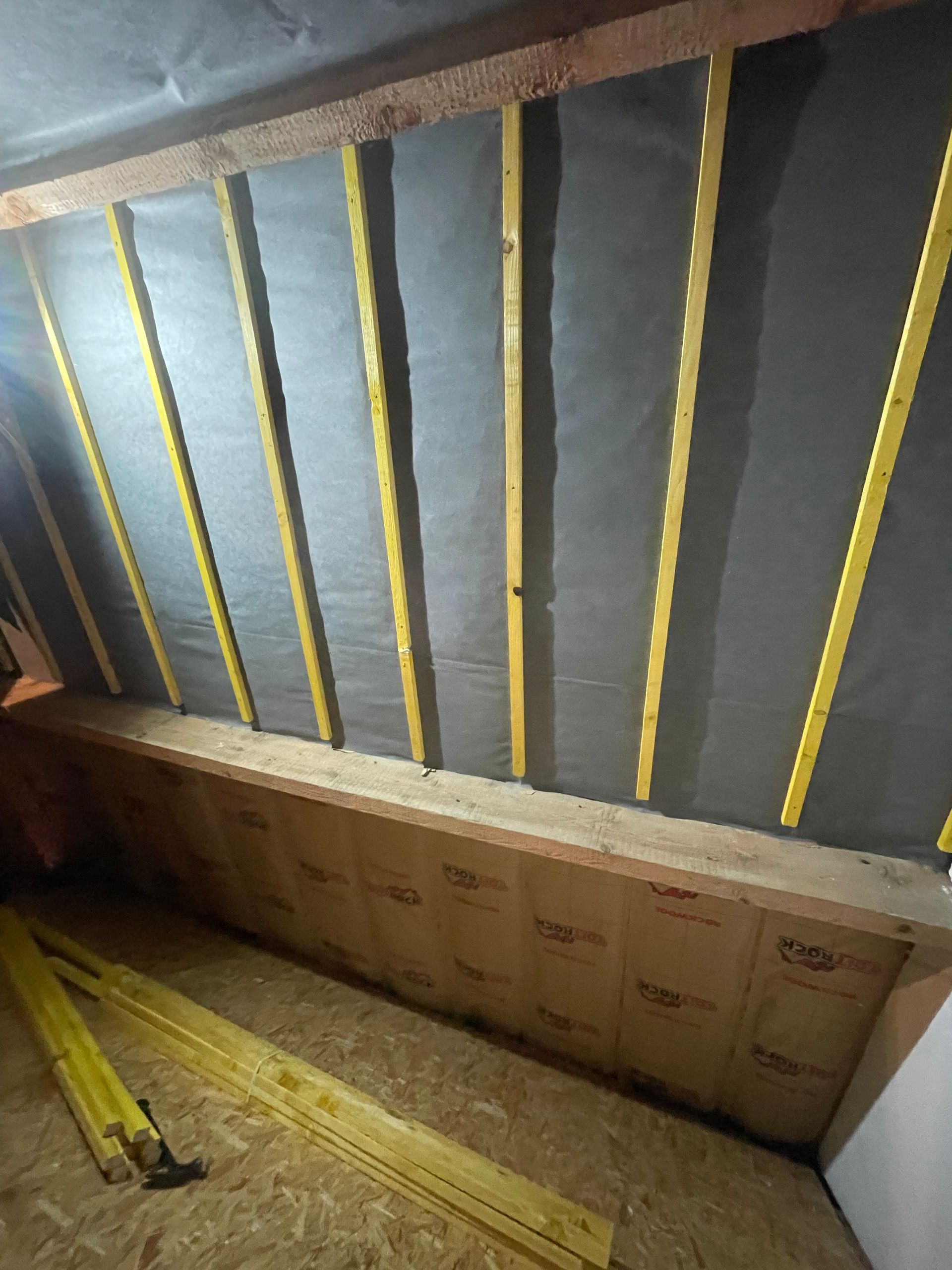 Construction d'une ossature dans un grenier, avec des montants muraux verticaux contre une membrane sombre et un plancher isolé.