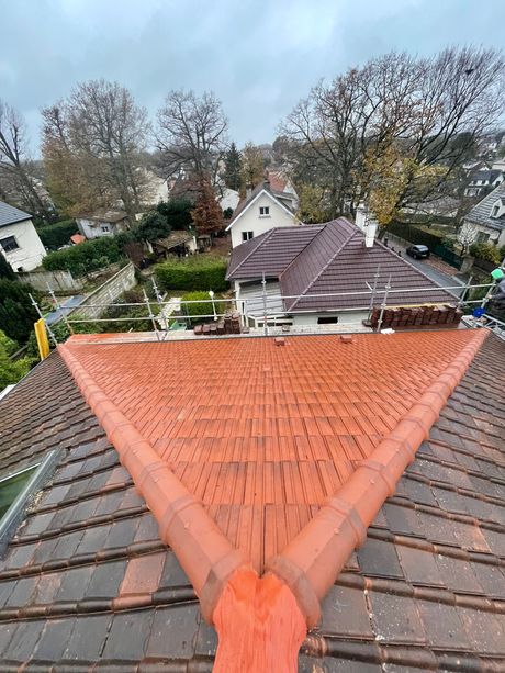 Une section triangulaire de tuiles de terre cuite neuves, d'un orange vif, entourée d'une toiture en tuiles plus anciennes, de couleur brun foncé.