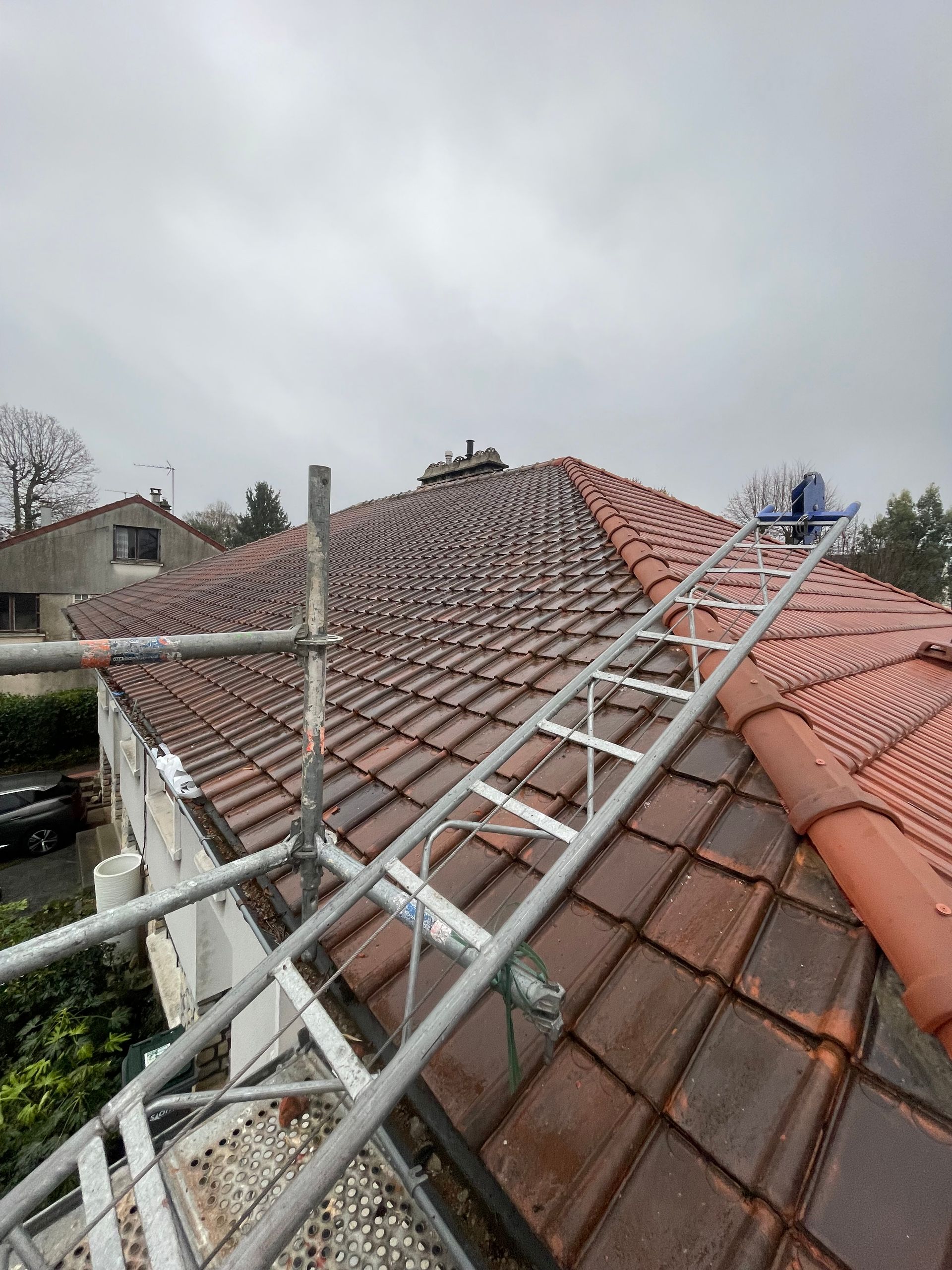 Un échafaudage et une échelle sont placés le long d'un toit de tuiles résidentiel sous un ciel nuageux.
