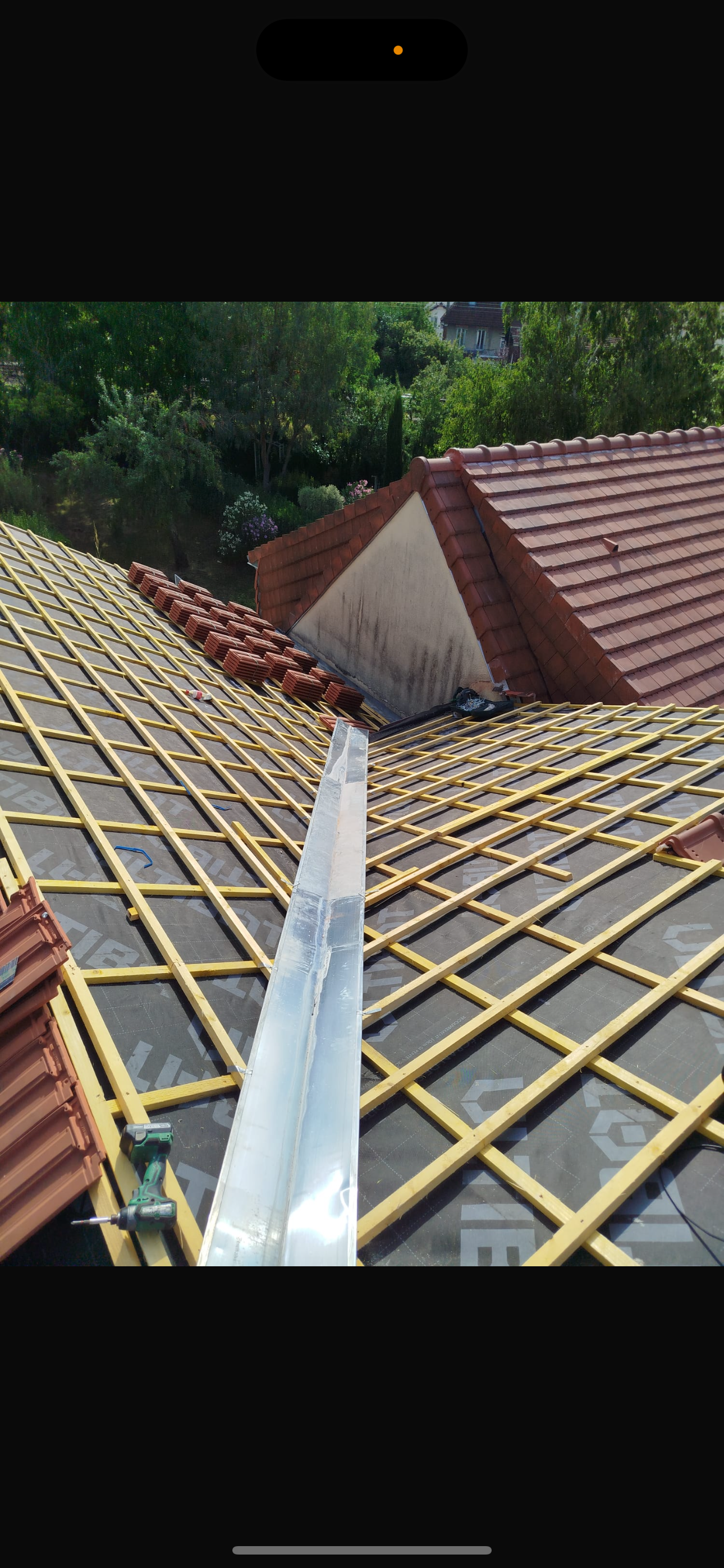 Vue d'un toit en construction avec une noue métallique installée sur une grille en bois, elle-même posée sur une sous-couche foncée.