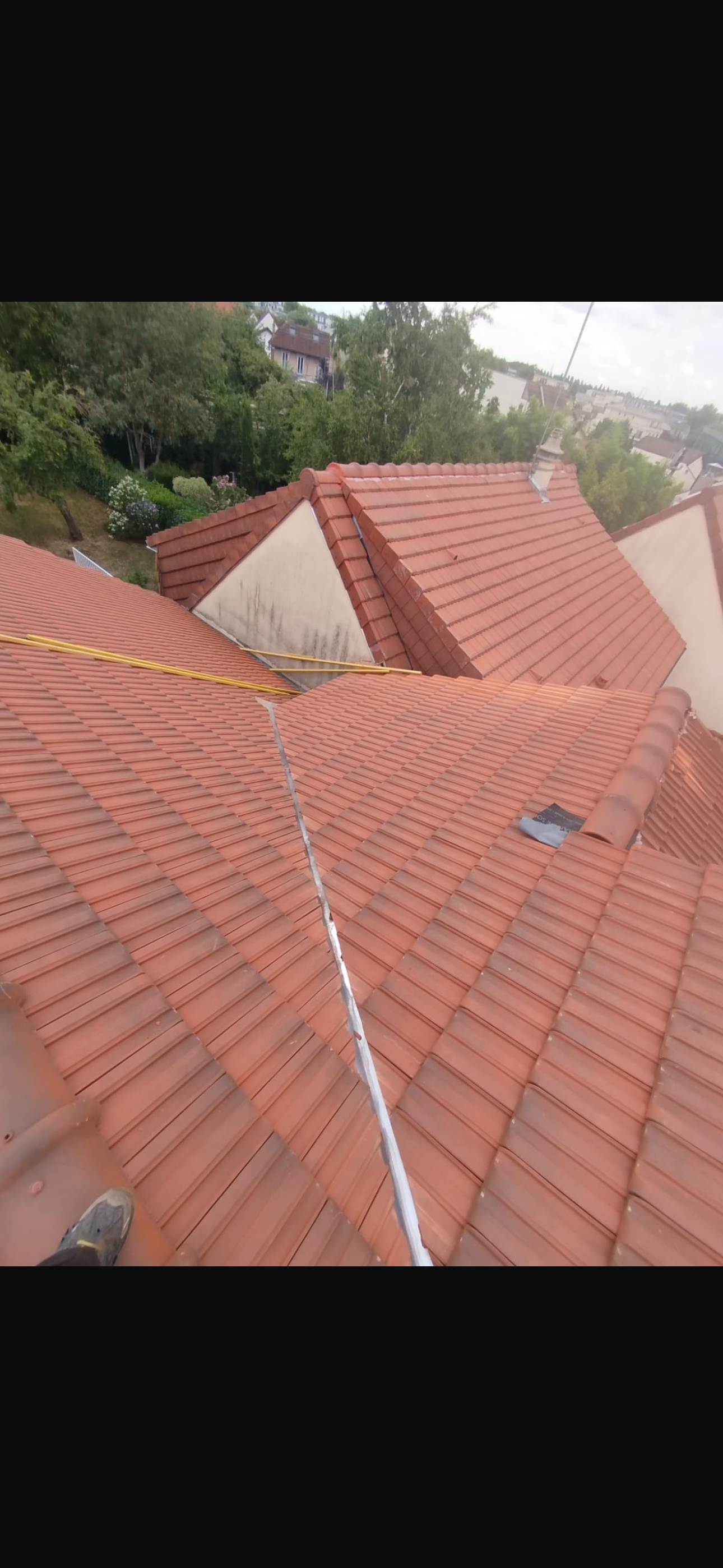 Vue en plongée d'un toit de tuiles rouges avec une faîtière blanche s'étendant verticalement vers une intersection complexe de pignons.