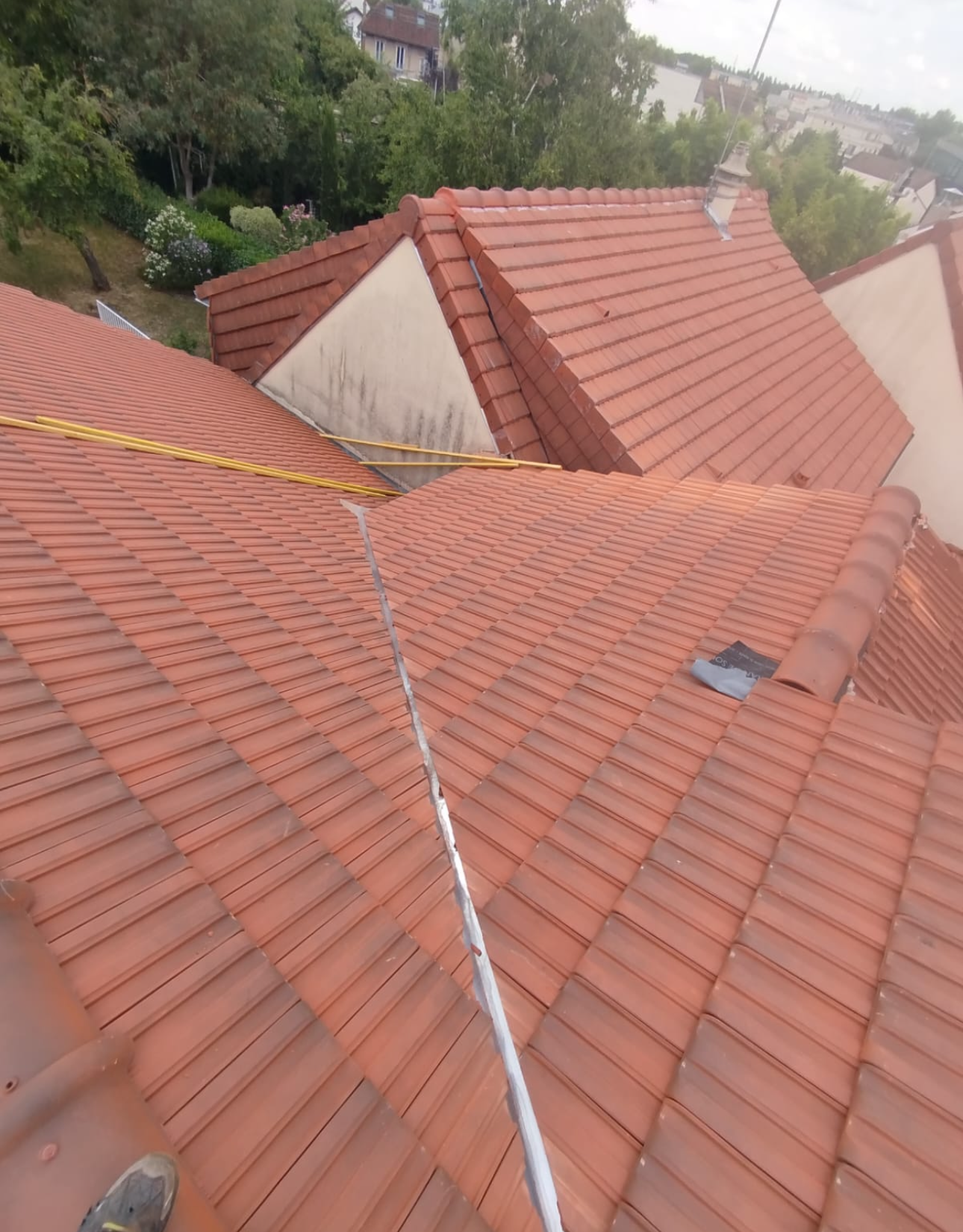 Vue en plongée d'un toit de tuiles rouges avec une arête centrale, des solins visibles et une ligne de sécurité jaune.