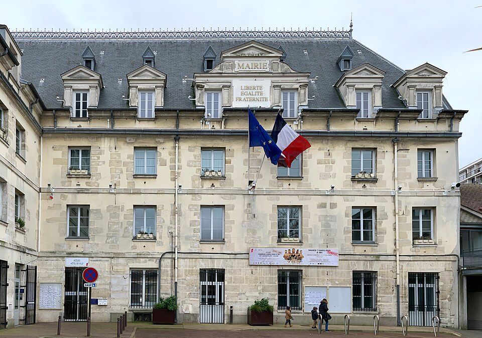 La mairie de Longjumeau, un bâtiment en pierre claire avec un toit mansardé, arbore les drapeaux français et européens.