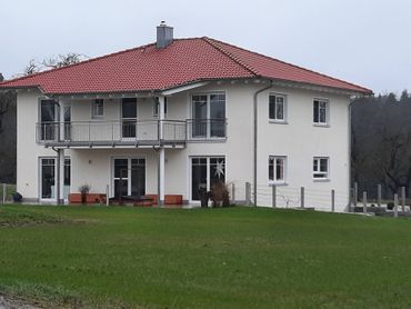 Mehrfamilienhaus mit rotem Dach umgeben von Wiese