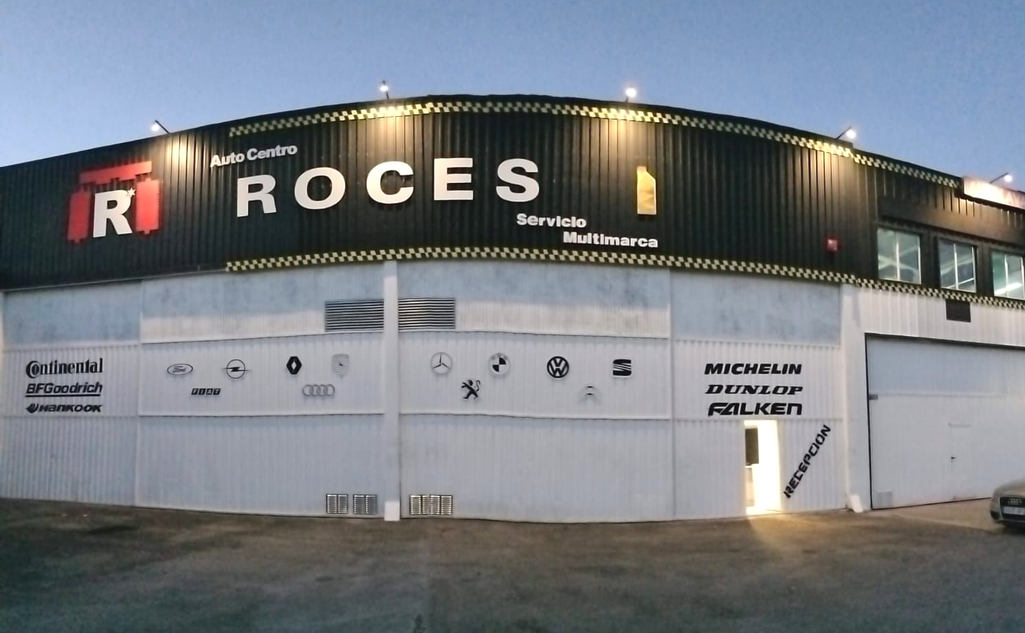 Exterior del taller mecánico Roces con cartel grande, varios logotipos de marcas de automóviles y marcas de neumáticos.