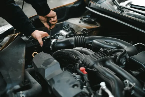 Mecánico trabajando en el motor de un automóvil; manos utilizando una herramienta en un compartimiento oscuro del motor.