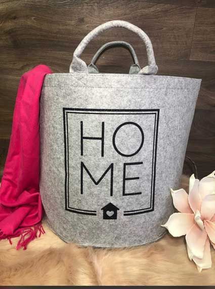 Ein Wäschekorb mit der Aufschrift „Home“ steht neben einem rosa Schal auf einem Tisch.