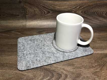 Eine weiße Tasse steht auf einem grauen Untersetzer auf einem Holztisch.