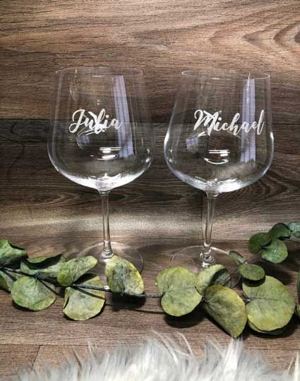 Auf einem Holztisch stehen zwei Weingläser mit den Namen Julia und Michael darauf.