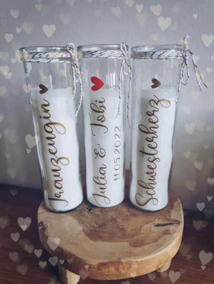 Auf einem Holztisch stehen drei Kerzen mit Namen darauf.