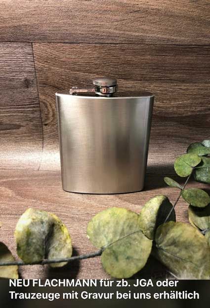 Eine Edelstahlflasche steht auf einem Holztisch neben Blättern.