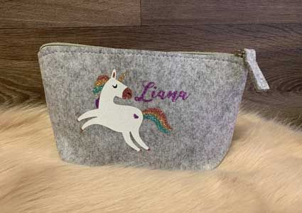 Eine Kosmetiktasche mit einem Einhorn und dem Namen Liana darauf gestickt.