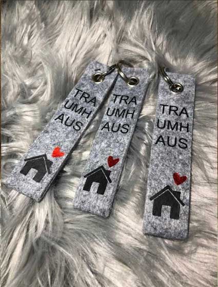 Drei Schlüsselanhänger mit Häusern und Herzen darauf liegen auf einer pelzigen Oberfläche.