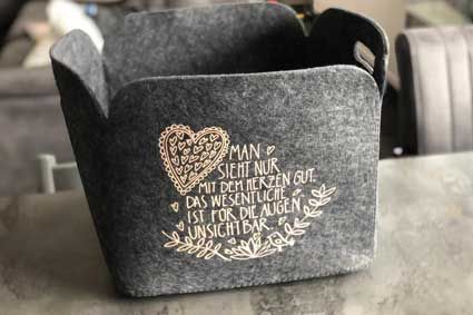 Auf einem Tisch steht ein grauer Korb mit einem Herz darauf.