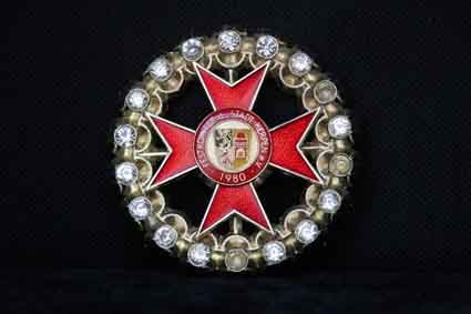 Eine Brosche mit einem roten Kreuz und Diamanten auf schwarzem Hintergrund.