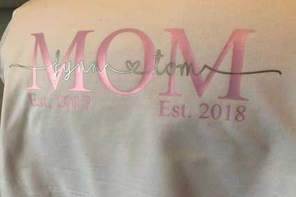 Die Rückseite eines weißen T-Shirts mit der aufgestickten Aufschrift „Mama“.