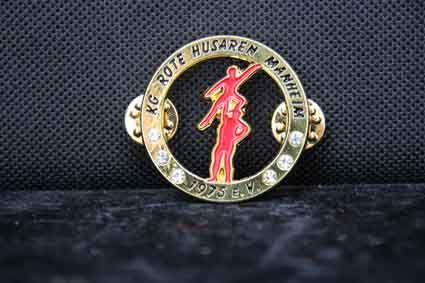 Eine goldene Anstecknadel mit einer roten Figur in einem Kreis auf schwarzem Hintergrund.