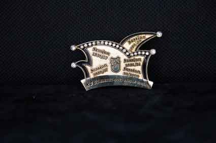 Auf einer schwarzen Oberfläche sitzt eine Brosche in Form einer Narrenmütze.