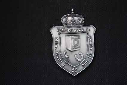 Ein silbernes Abzeichen mit einer Krone darauf auf schwarzem Hintergrund.