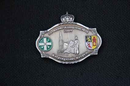 Eine silberne Gürtelschnalle mit einer Krone darauf auf schwarzem Hintergrund.