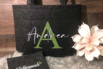 Eine schwarze Einkaufstasche mit dem Buchstaben A darauf liegt neben einer Blume.