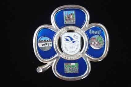 Eine Brosche in Form eines Kleeblatts mit vier Blättern auf schwarzem Hintergrund.