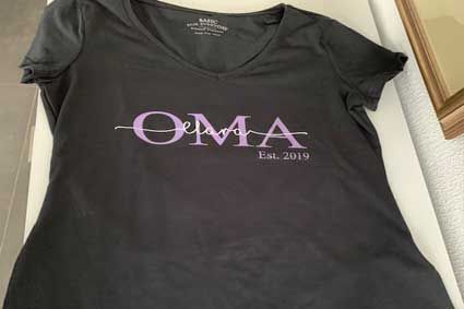 Auf einem Tisch liegt ein schwarzes T-Shirt mit violetter Schrift.