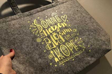 Eine Person hält eine graue Einkaufstasche mit gelber Schrift darauf.