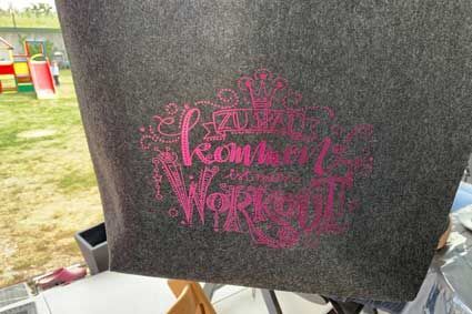 Auf einem Tisch liegt eine graue Einkaufstasche mit rosa Schrift.