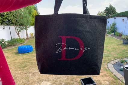 Eine schwarze Einkaufstasche mit dem Buchstaben D hängt in einem Garten.