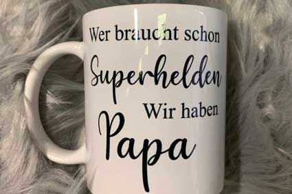 A white coffee mug with the words `` wer braucht schon superhelden wir haben papa '' written on it.
