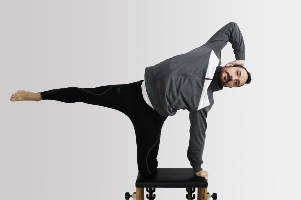 Persona realizando una postura de equilibrio lateral sobre una plataforma contra un fondo blanco.