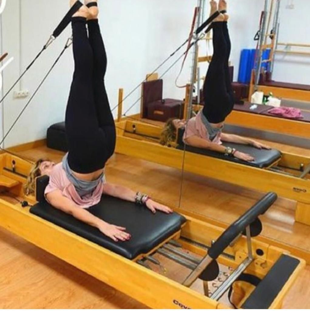 Persona realizando una elevación vertical de piernas de pilates en una máquina reformer en un estudio con espejos.