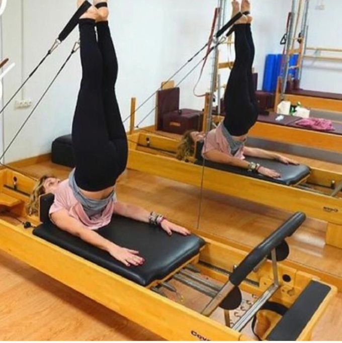 Persona realizando una inversión de Pilates en un reformer en un estudio con espejos y paredes de madera.