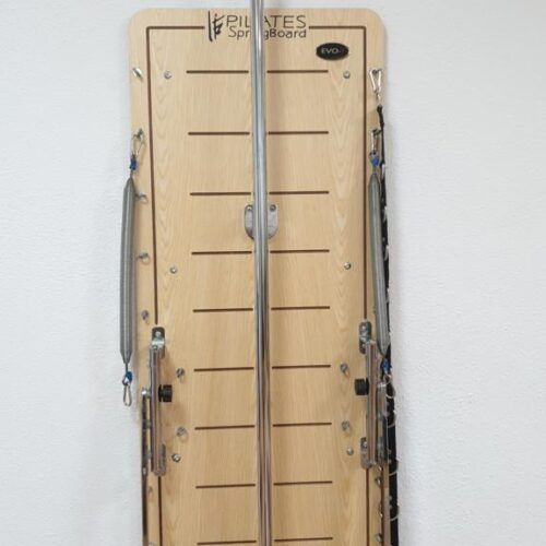 Reformer de Pilates de madera con correas negras contra una pared blanca.