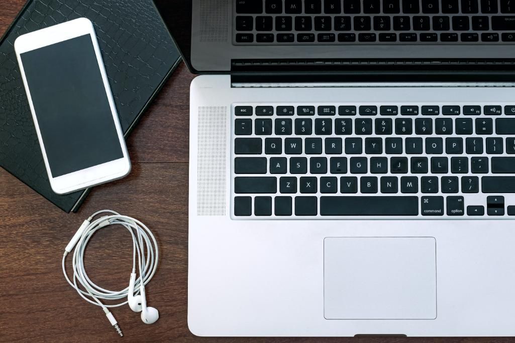 Un ordenador portátil, un teléfono inteligente y unos auriculares con cable están sobre un escritorio 