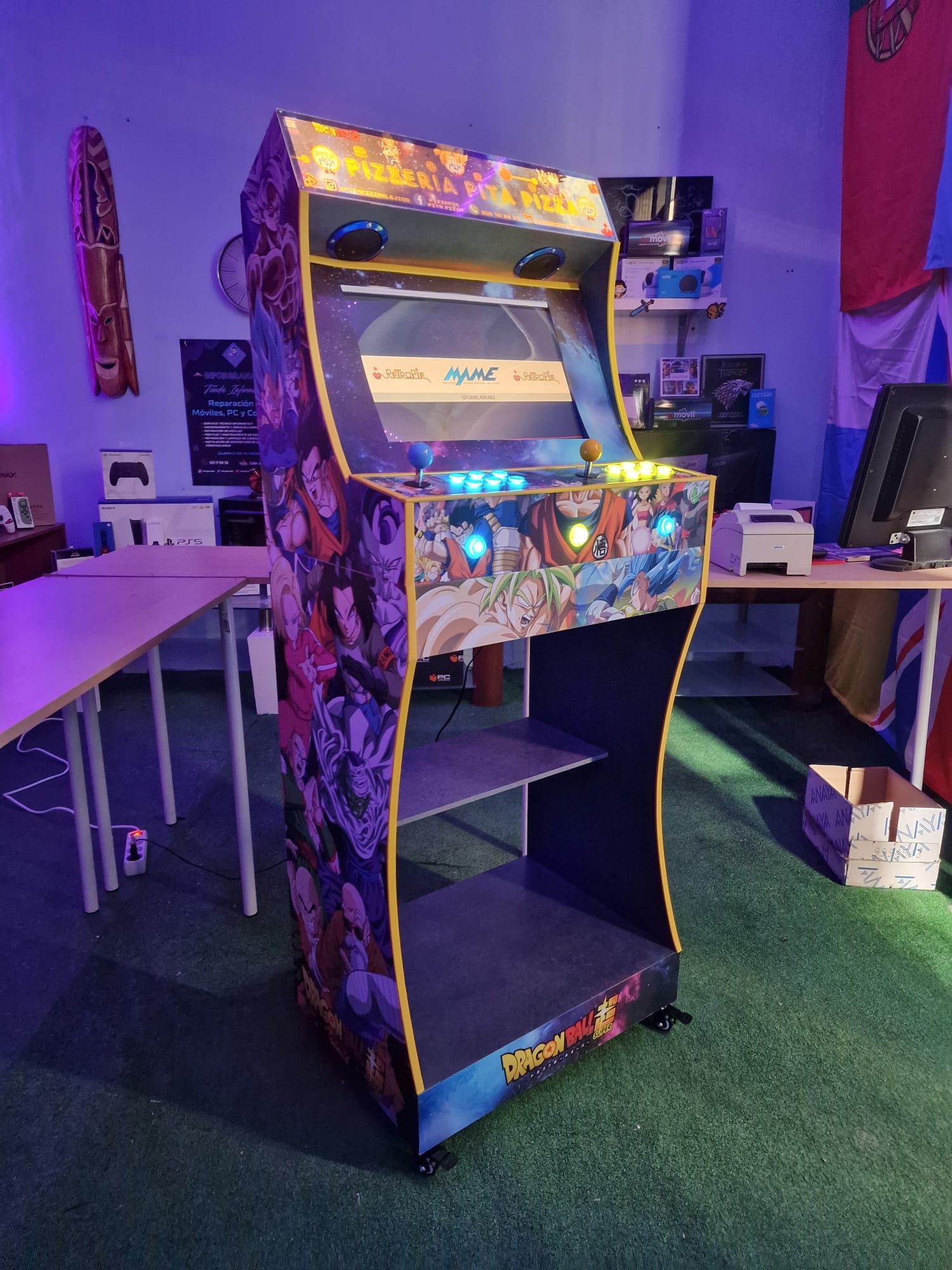 Máquina recreativa colorida en una habitación con iluminación púrpura y mesas cerca