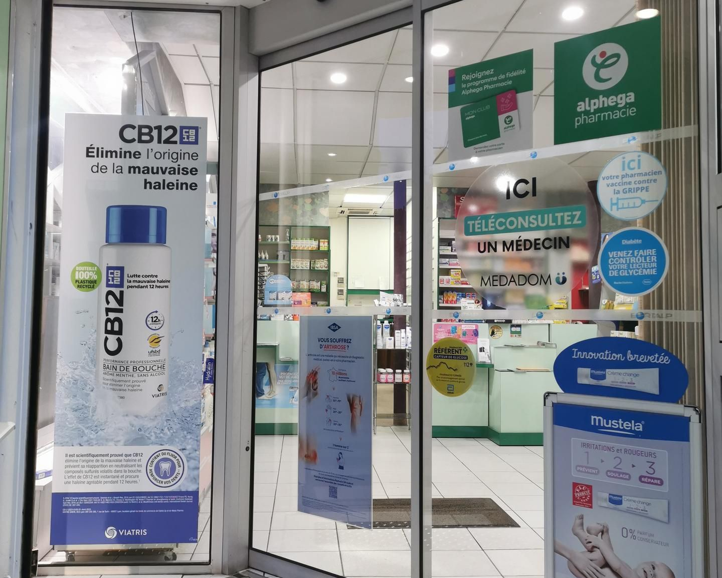 Entrée de la pharmacie avec portes coulissantes en verre ; publicités visibles.
