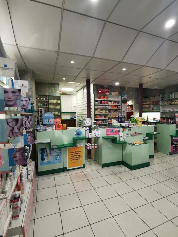 Intérieur d'une pharmacie avec comptoirs verts, étagères de produits et sol carrelé.