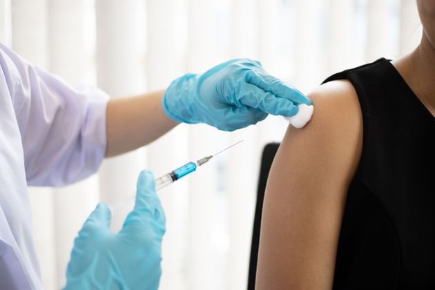 Personne recevant une injection de vaccin dans le bras. Personnel soignant portant des gants bleus et une blouse de laboratoire.